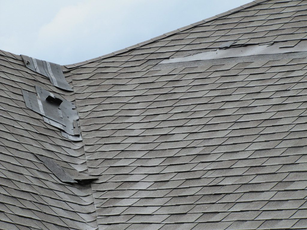 Hail storm damage on an asphalt shingle roof, shingles torn along the ridge