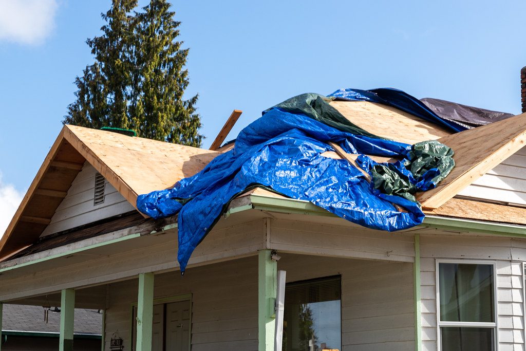 Storm-torn asphalt shingles exposing the wooden roof deck beneath, under dark clouds